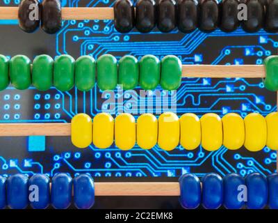 Close-up of a wooden abacus with colorful beads in front of traces of an electronic circuit board. Stock Photo