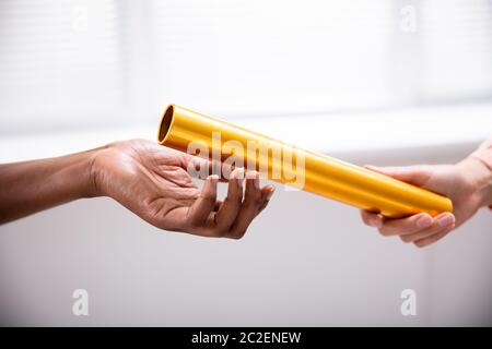 Close-up Of A Hand Passing Golden Relay Baton To African Woman's Hand Stock Photo