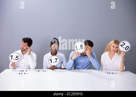 Disappointed Business People Showing Low Score Cards Sitting Against Grey Wall Stock Photo