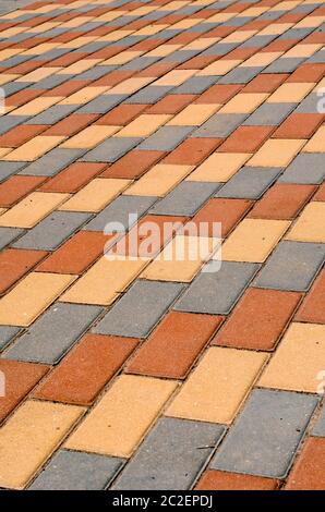 City street paved with three-color paving slabs. Sidewalk with gray, yellow and red cement rectangular tiles. Multi-colored paints of a modern city. S Stock Photo