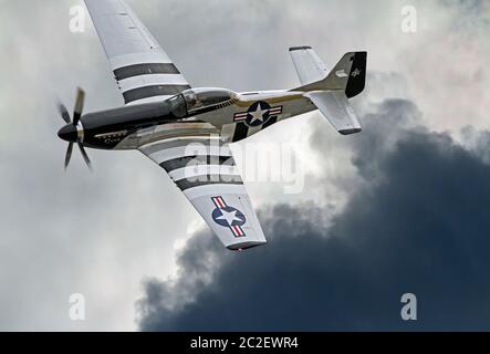 A World War II-era P-51 Mustang fighter airplane in flight banks over dramatic clouds. Stock Photo