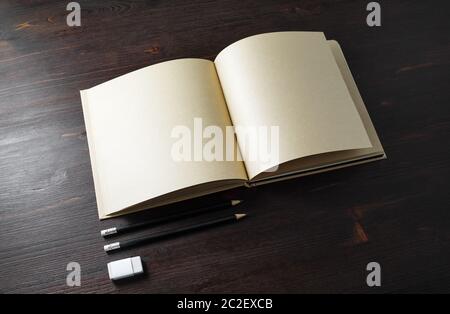 Opened book or booklet with blank kraft paper pages, pencils and eraser on wood table background. Stock Photo