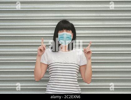 woman wearing medical mask thoughtful pointing  with two forefinger up and looking above  outdoor Stock Photo