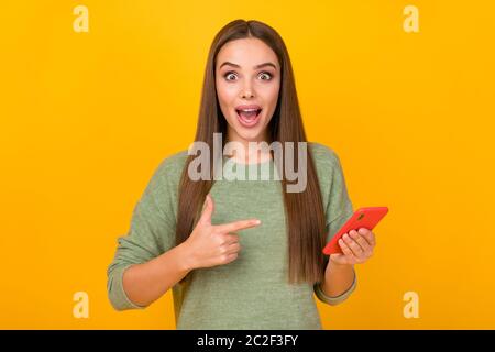 Portrait of astonished crazy girl blogger use cellphone indicate incredible ads promotion point index finger scream wow omg wear sweater isolated over Stock Photo