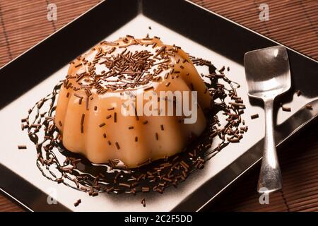 Caramel pudding dessert decorated with sweet sauce and chocolate crumbs on black square plate. Stock Photo