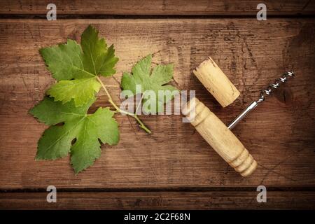 A vine leaf with a vintage corkscrew and a cork, shot from above on a dark rustic wooden background Stock Photo