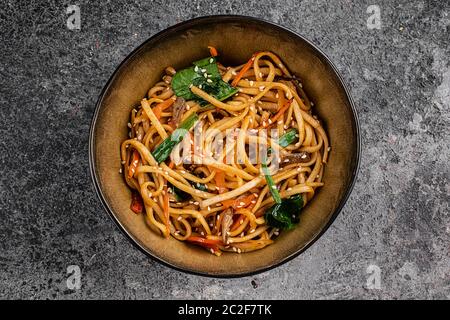 fried soba noodles with mushrooms, broccoli, carrots, peppers closeup on a plate on a table. Vertical top view from above Stock Photo