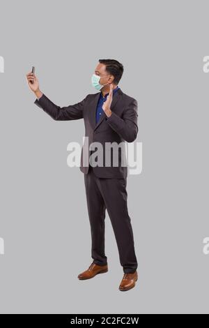 Businessman Having Video Call on Phone Wearing Medical Mask Isolated. Indian Man Businessman Video Call. Business Online. Businessman Using Phone Stock Photo