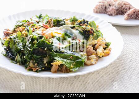 A white plate of delicious Stir-Fried Baegu Leaves or Melinjo with Eggs, served with steamed rice. Stock Photo