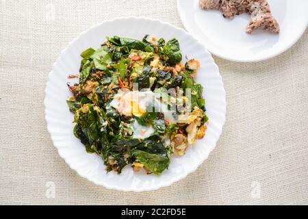 A white plate of delicious Stir-Fried Baegu Leaves or Melinjo with Eggs, served with steamed rice. Stock Photo