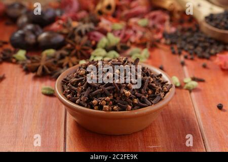 Cloves  spice ,aromatic flower buds arranged in a earthenware bowl with wooden background selective focus Stock Photo