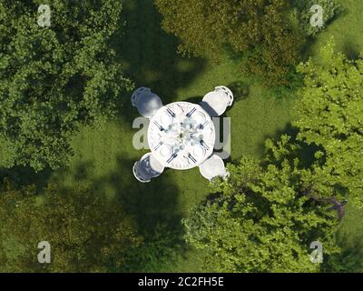 Round dining table in a classic style stands on the grass in the forest among the trees. Exquisite aristocratic table setting outdoors surrounded by a Stock Photo