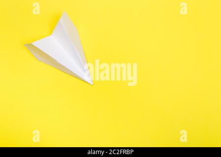 Flat lay of white paper plane and blank paper on yellow color background.