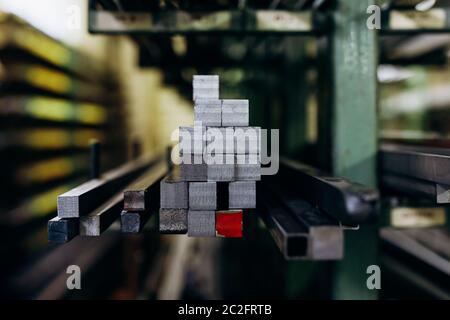 Steel square shaped rods in different sizes lying on storage shelves. Details of metallurgical plant. Close up, copy space. Stock Photo