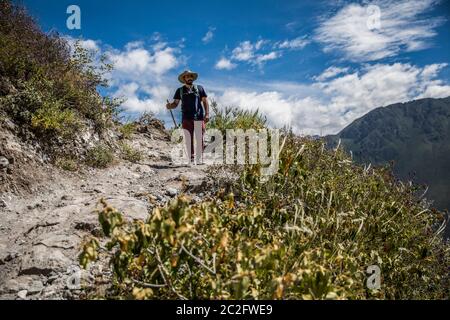 young man is walking in a canyon, big mountains, clouds and blue sky Stock Photo