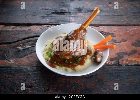 Turkish lamb shank in dark sauce with potato puree and vegetables isolated on rustic wooden table Stock Photo