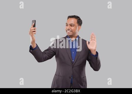 Businessman Having Video Call on Phone Waving Isolated. Indian Man Businessman Video Call. Business Online. Businessman Using Phone. Indian Business Stock Photo