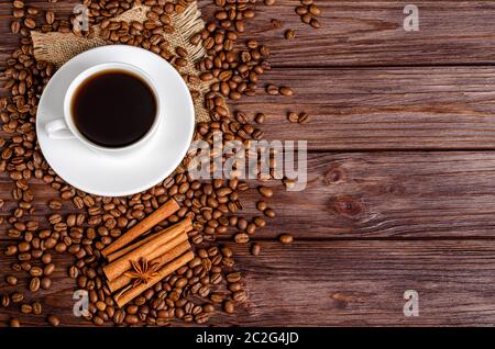 A cup of black aromatic coffee in a white cup with roasted coffee beans arabica, anise stars, cinnamon sticks on a wooden background. Copy space. View Stock Photo