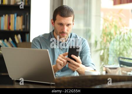 Serious man using smart phone and laptop sitting in a coffee shop Stock Photo