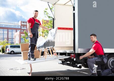 Two Young Male Movers Loading The Cardboard Boxes And Furniture In Moving Truck On Street Stock Photo