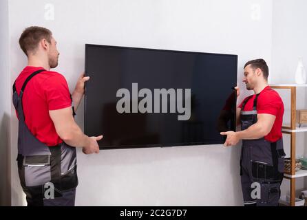 Movers Fixing The Large Flat LCD Television On Wall In The Living Room Stock Photo