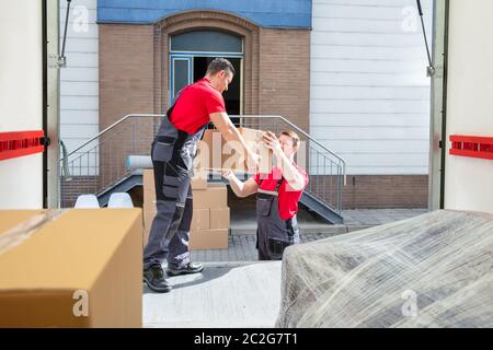 Young Male Movers Unloading The Cardboard Boxes In The Van Outside The House Stock Photo