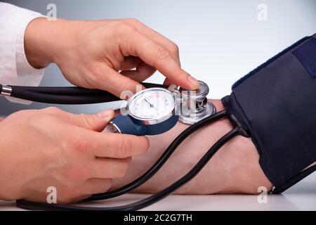 Close-up Of Doctor Checking Blood Pressure Of The Male Patient On Table Against Gray Background Stock Photo