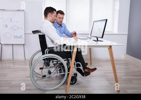 Young Businessman Sitting Near The Disabled Male Colleague Working Together On Computer Stock Photo