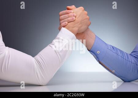 Close-up Of Two Businessmen Competing In Arm Wrestling On Reflective Desk Against Grey Background Stock Photo