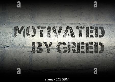 motivated by greed stencil print on the grunge white brick wall Stock Photo