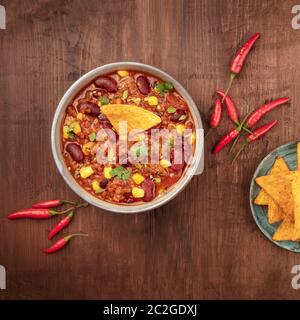 Chili con carne with chilli peppers and nachos, overhead square shot on a dark rustic wooden background Stock Photo