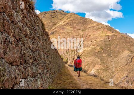 Indigenous Peruvian Quechua woman in traditional clothing walking along the inca agriculture terraces of Pisac, Cusco Province, Peru. Copy Space. Stock Photo