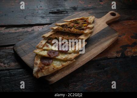 Turkish pide with sausage, beef and vegetables isolated on rustic wooden table