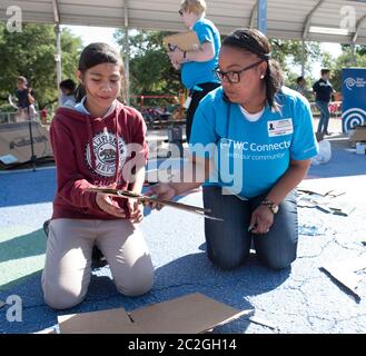 Austin Texas USA, April 20 2016: Adult volunteer advises students at Cedars International Academy, competing in the Earth Day Cardboard Challenge program at Cedars International Academy, as they design and build a science display out of cardboard and other simple recycled products. The event was held on Earth Day. ©Bob Daemmrich Stock Photo