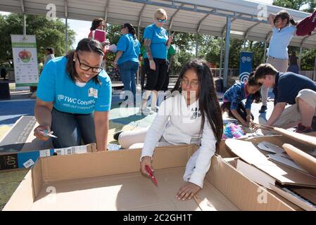 Austin Texas USA, April 20 2016: Adult volunteer advises students at Cedars International Academy, competing in the Earth Day Cardboard Challenge program at Cedars International Academy, as they design and build a science display out of cardboard and other simple recycled products. The event was held on Earth Day. ©Bob Daemmrich Stock Photo
