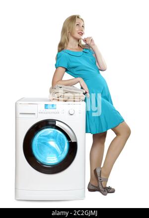 happy young woman in a bright dress joyfully looks up. Leans on a new washing machine with a stack o Stock Photo