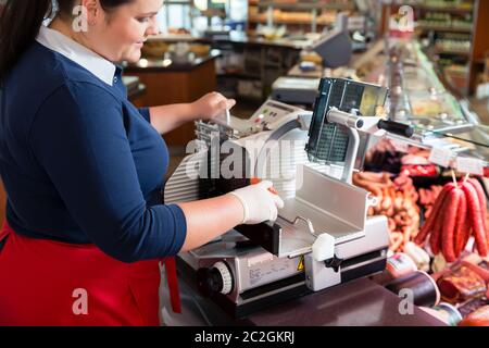 Woman in butcher shop cutting bacon or ham with machine Stock Photo