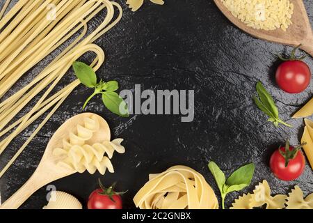 Italian food design template. Pasta, tomatoes and basil, a flat lay frame on a black background with a place for text. Spaghetti Stock Photo