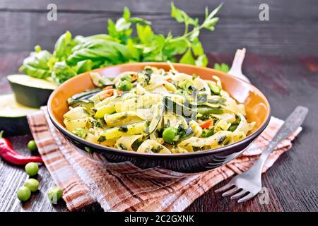 Tagliatelle pasta with zucchini, green peas, asparagus beans, hot peppers and spinach in  kitchen towel, garlic, fork and basil on dark wooden board Stock Photo