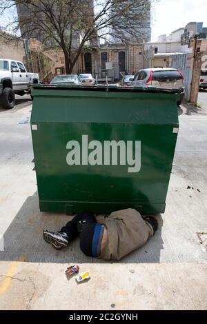 Homeless man sleeping by dumpster - A homeless man appears to be sleeping behind a trash receptacle in downtown Austin and is awakened by a police officer following a complaint by a landowner.  No arrests were made or tickets issued.  March 28, 2014© Bob Daemmrich Stock Photo