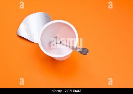 empty clean yogurt cup with spoon on an orange background Stock Photo