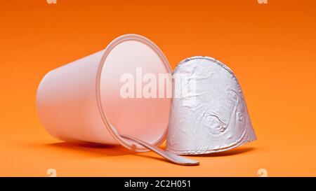 empty clean yogurt cup with spoon on an orange background Stock Photo