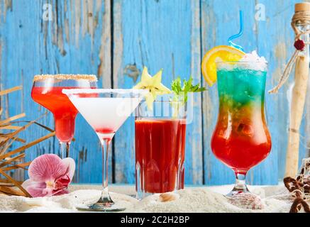 Assorted colorful cocktails with a martini and bloody Mary on white beach sand against a rustic weathered blue wood background Stock Photo