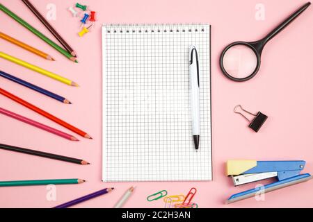 colored pencils, stationery, paper notebook with pen and magnifier on pink isolated background. top view. flat lay. mockup Stock Photo