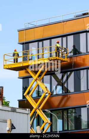 two workers inspect the facade of the building on a scissor lift platform Stock Photo