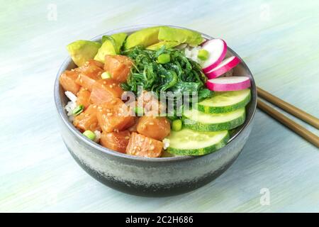 A bowl of salmon poke with avocado, wakame and cucumber on a teal blue background Stock Photo
