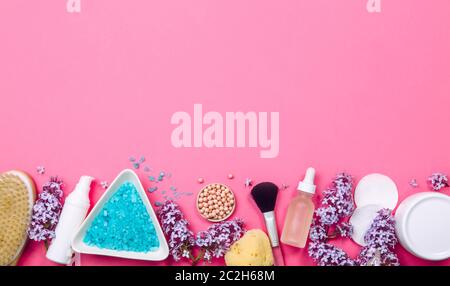 Flat lay view of various beauty spa products on pastel pink background with lot of copy space. Highlighter pearls, make up brush, lilac flowers. Stock Photo