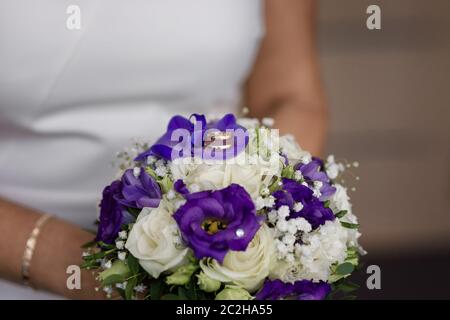 Wedding rings lying on the bride's bouquet of white and purple flowers in the hands of the bride Stock Photo