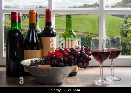 Composition with two wineglasses, grapes and bottles of red wine, window at background Stock Photo