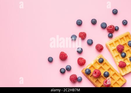 Waffles with blueberries and raspberries on pink background. Top view. Stock Photo